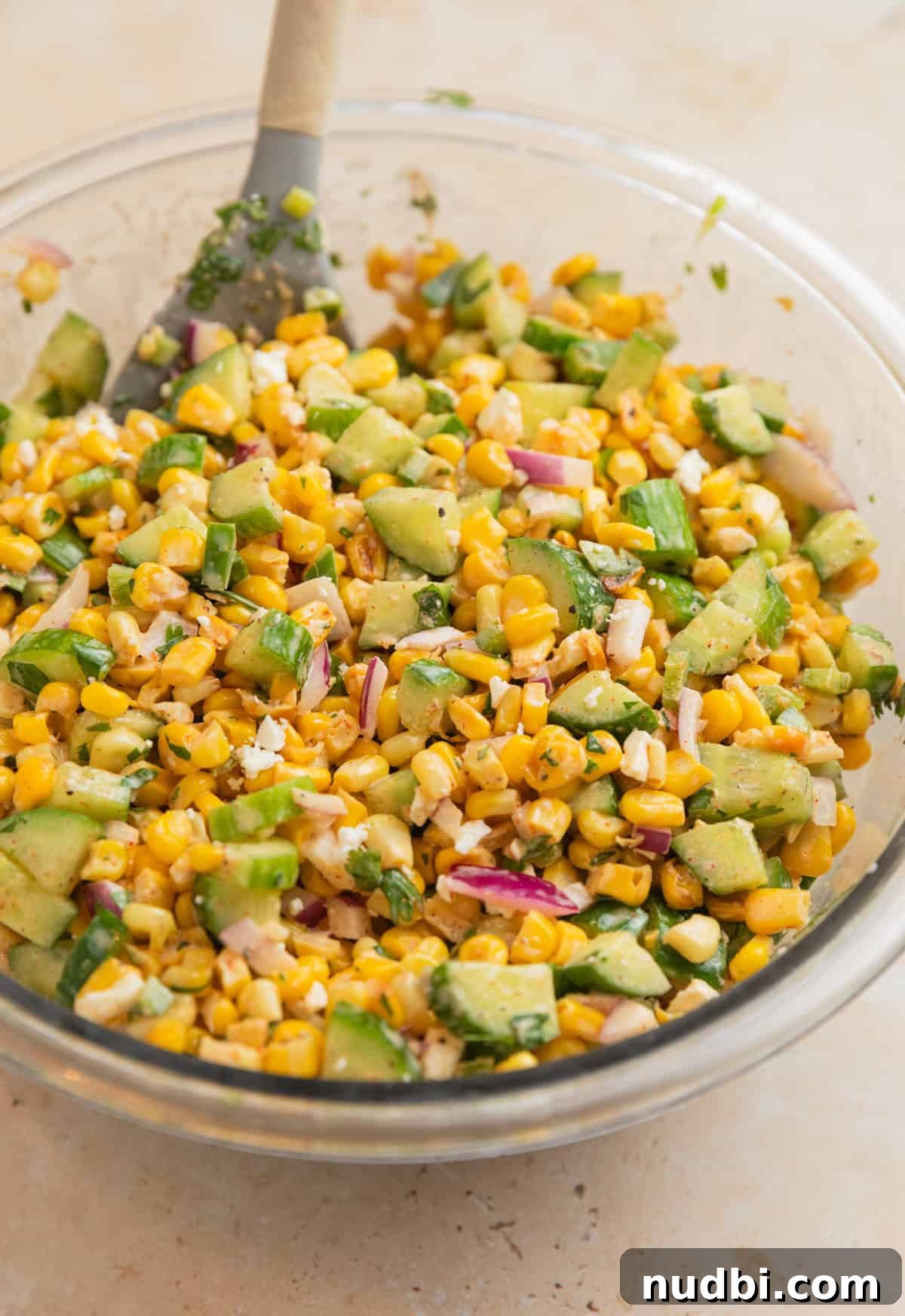 Cucumber and Sweet Corn Salad with Herb Vinaigrette 7 Prepped cucumber corn salad in glass bowl with spoon.