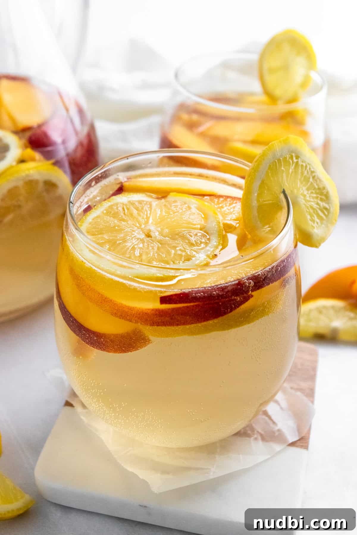 Ginger Peach White Sangria Recipe for Summer Entertaining 2 Ginger peach white sangria in glass with lemon slice on coaster.