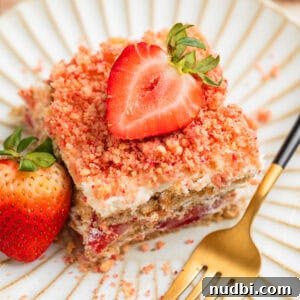 Strawberry Cream Cheese Icebox Cake Recipe for Summer Desserts 7 Layered strawberry icebox cake topped with strawberry crunch on plate with fresh strawberry garnish.