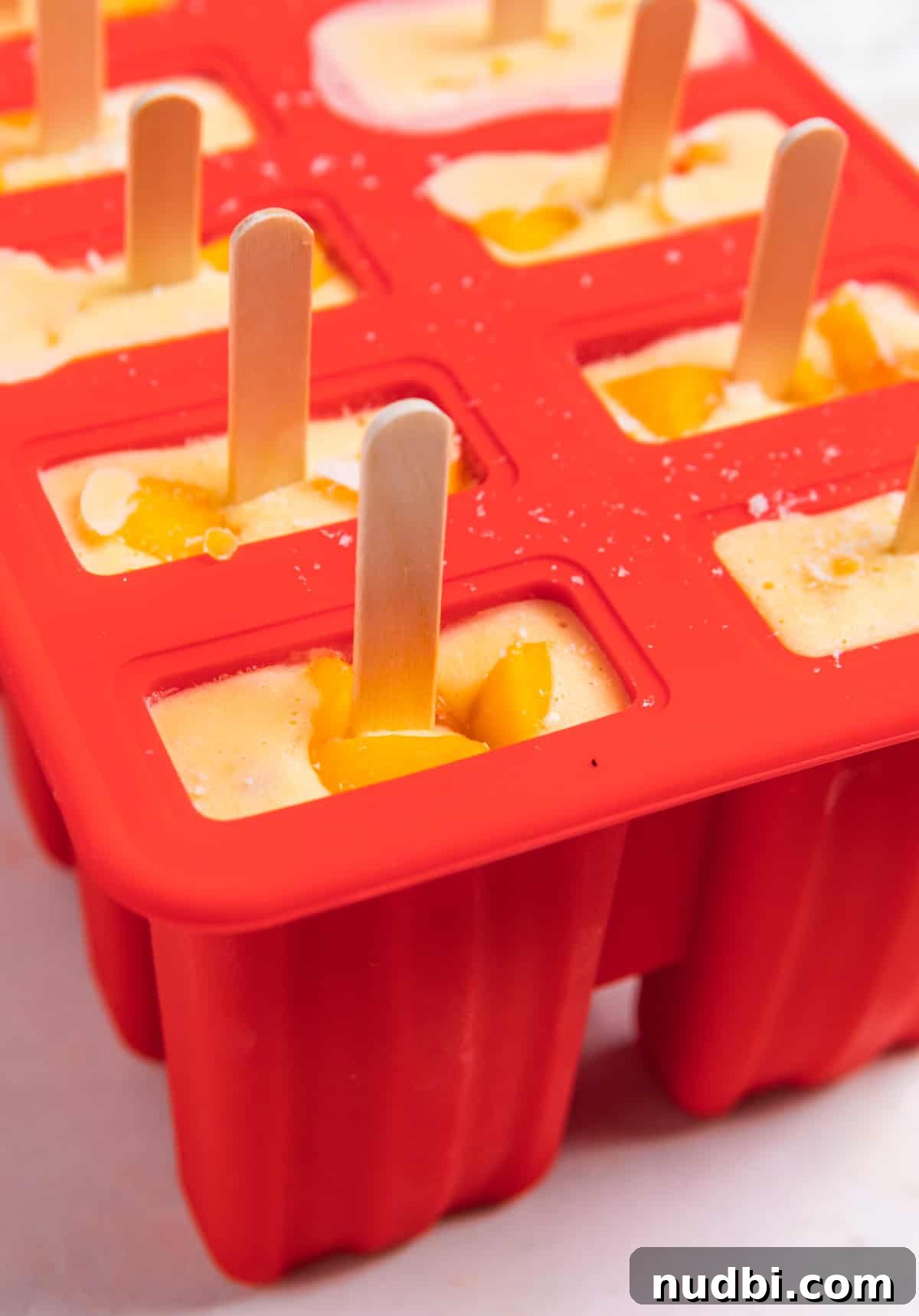 Popsicle mold filled with peaches and cream blended mixture and popsicle sticks inserted.