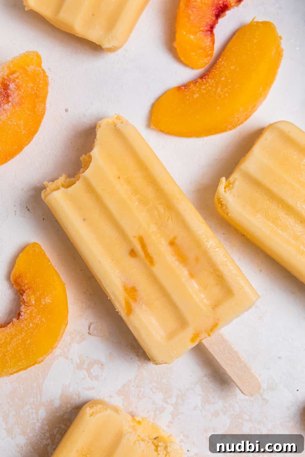Peach popsicle on counter with peach slices surrounding.