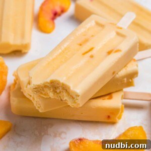 Creamy peach popsicles stacked with bite taken out of top popsicle.