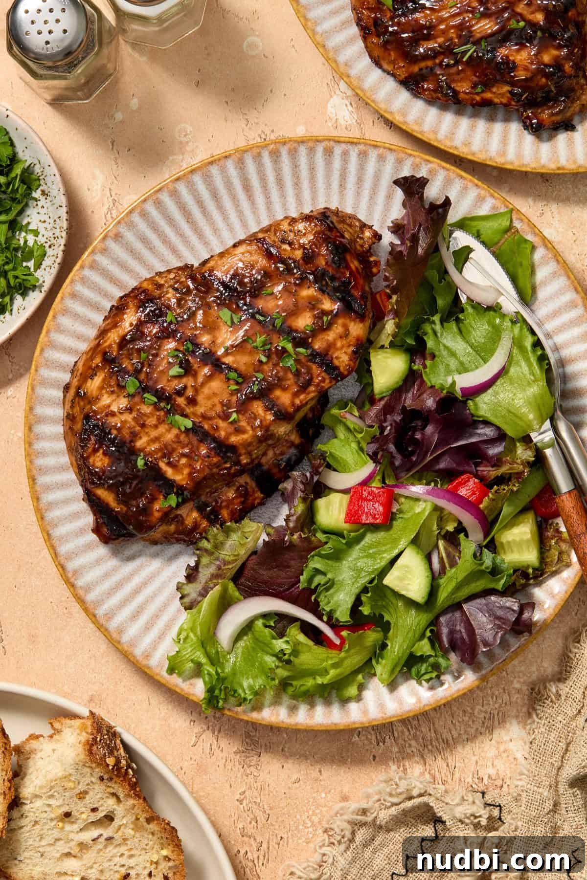 Balsamic grilled chicken on plate with salad and chopped parsley over top.