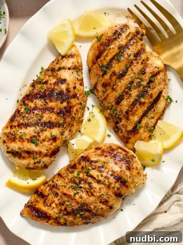 Grilled lemon pepper chicken on white serving platter with lemon wedges.