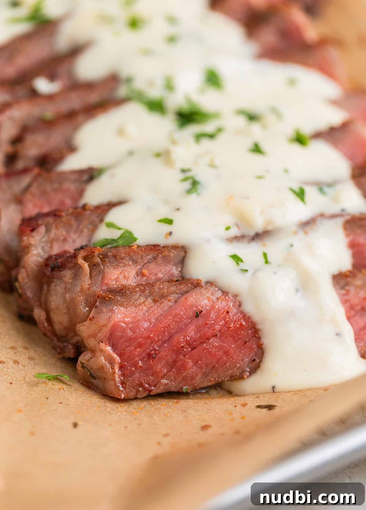 Grilled Ribeye with Creamy Gorgonzola Sauce Recipe 10 Sliced ribeye steak on parchment paper with cream sauce over top.