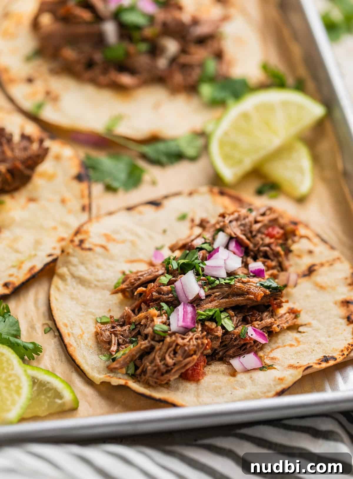 Slow-Cooker Shredded Beef Tacos Recipe for Tender, Flavorful Meat 2 Shredded beef tacos on parchment lined pan topped with onion and cilantro.
