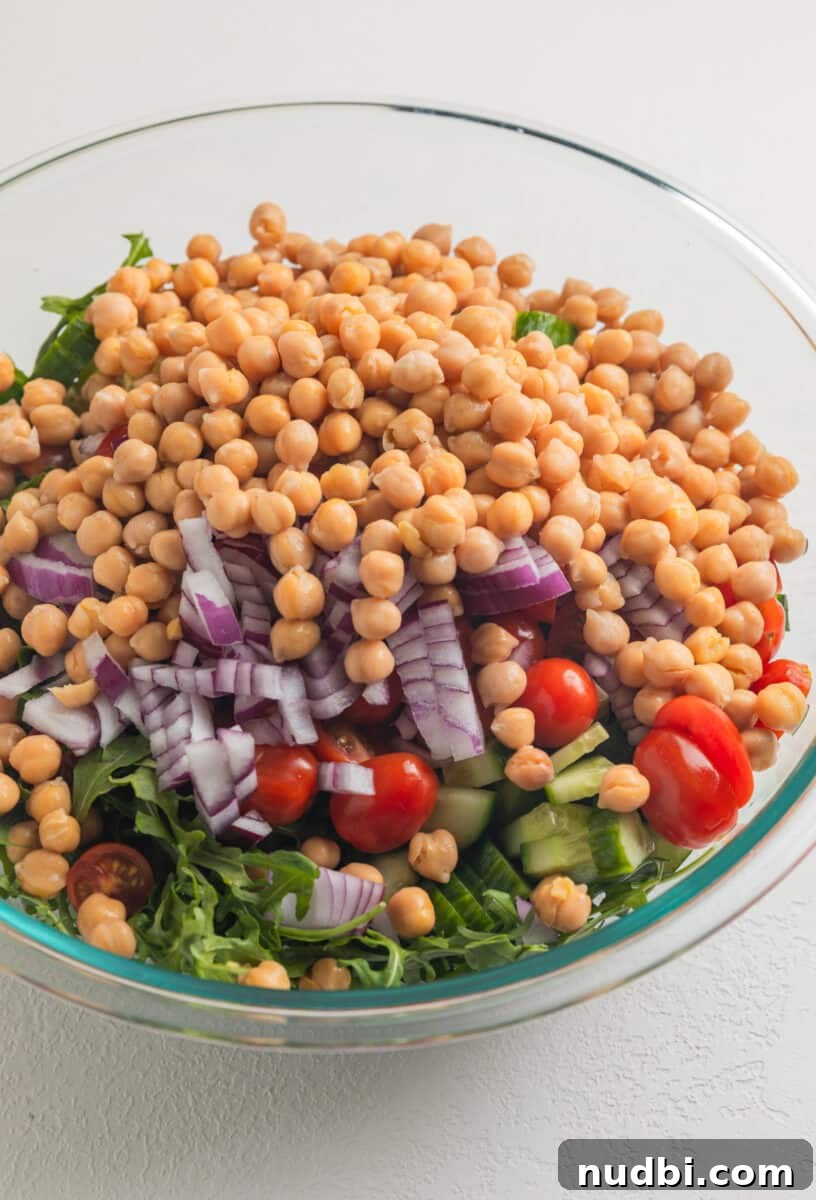 Creamy Chickpea and Avocado Salad with Lemon Dressing 4 Garbanzo beans, arugula, onion, tomato and cucumber in glass mixing bowl.