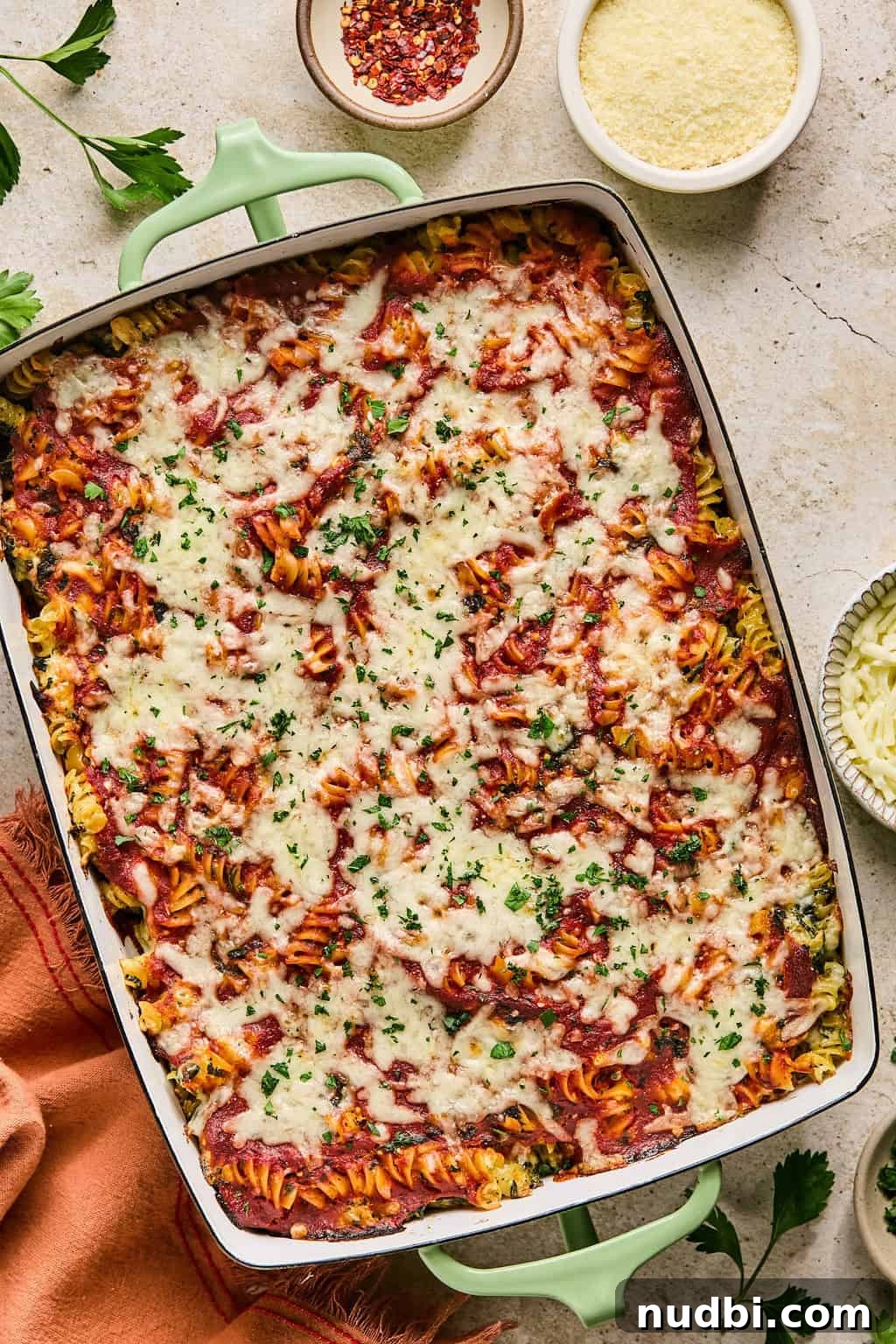 Spinach Baked Pasta with Creamy Cheese and Garlic 9 Baked pasta topped with fresh herbs and bowl of spices and cheese surrounding the dish.