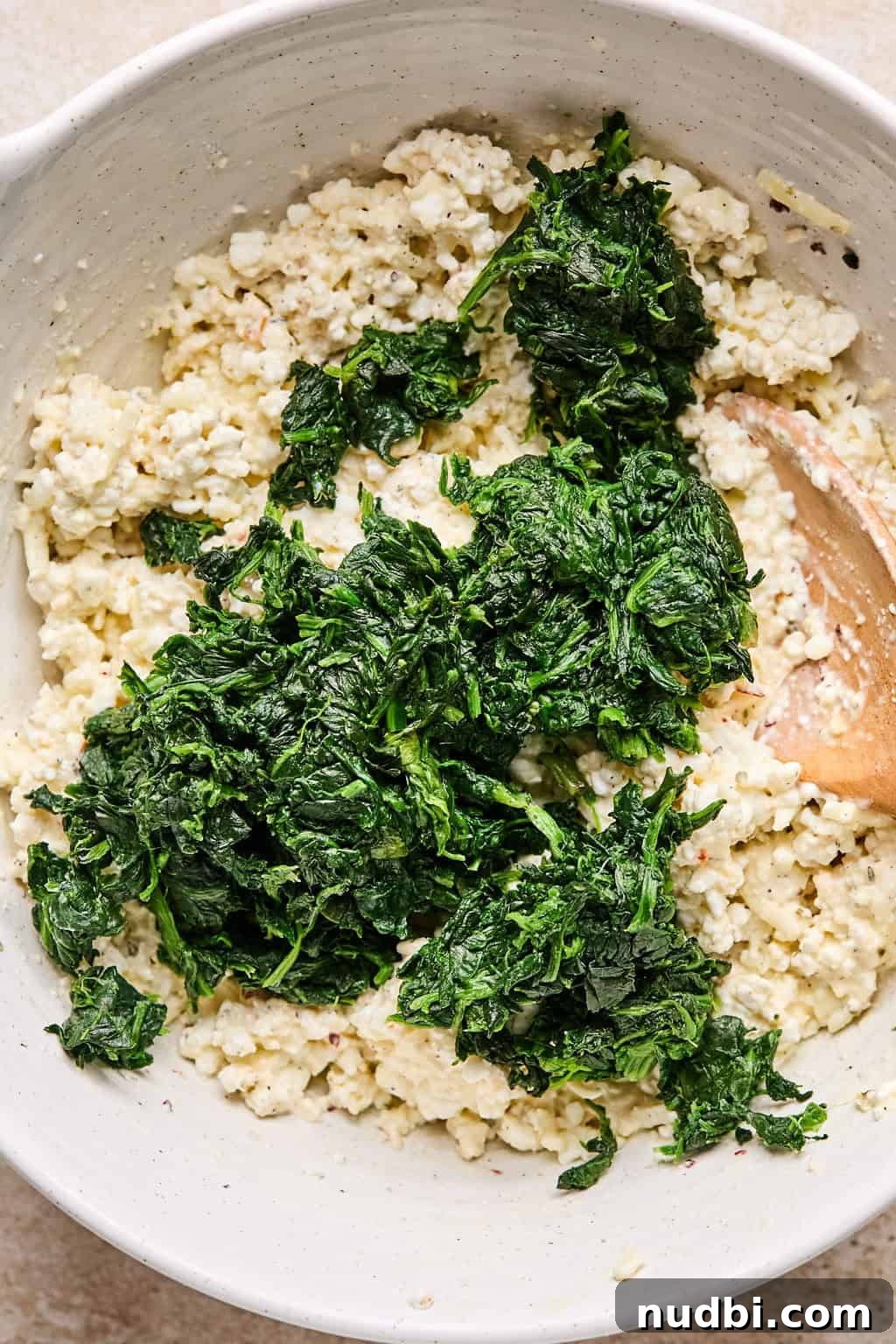 Spinach Baked Pasta with Creamy Cheese and Garlic 7 Spinach added to cottage cheese mixture in mixing bowl with wooden spoon.