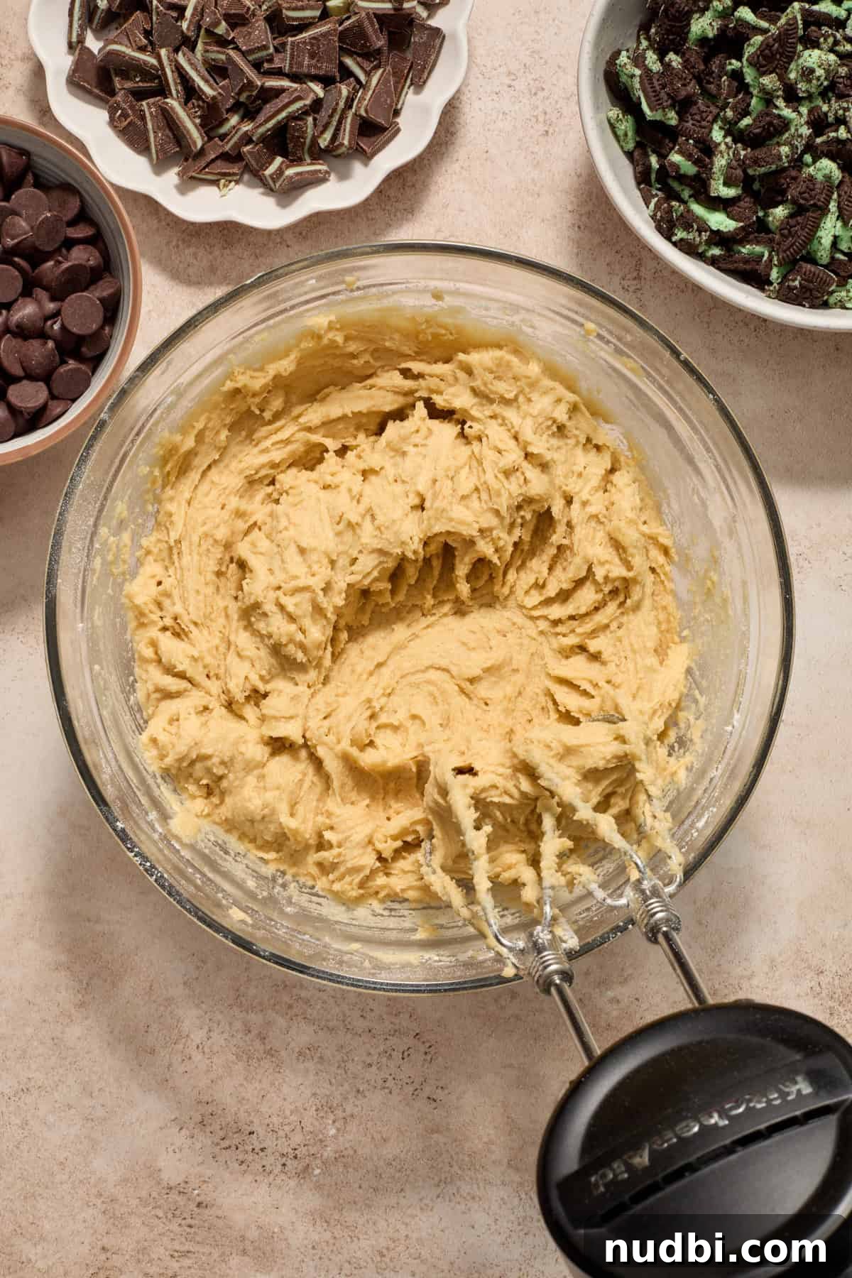 Chewy Mint Chocolate Chip Cookies Recipe for Perfect Cookies 9 Mint chocolate cookie dough in bowl with hand mixer surrounded by bowls with add-ins.