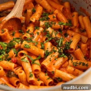 Creamy one pot tomato pasta in pot with wooden spoon.