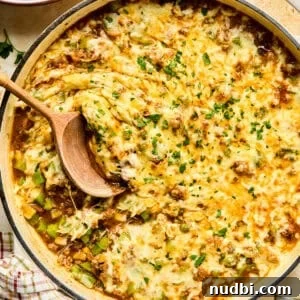 Cheese topped Philly cheesesteak skillet mixture in pan with wood spoon.