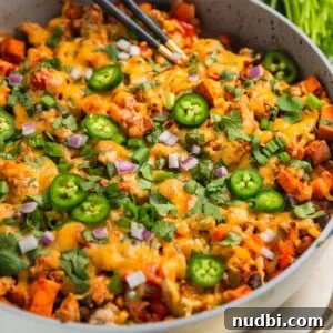 Ground turkey sweet potato skillet dinner in pan with spoons scooping into the skillet.