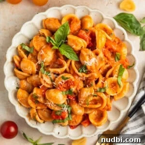Plate with cherry tomato pasta topped with fresh chopped basil and parmesan.