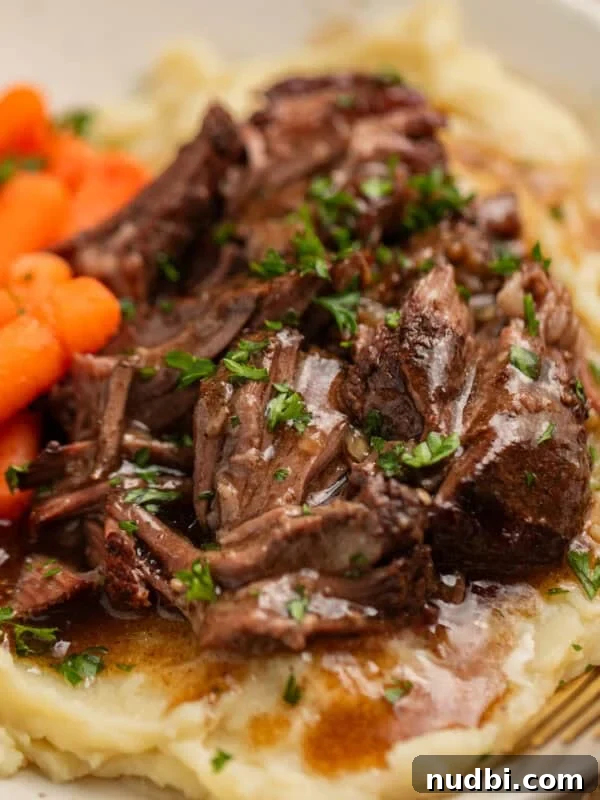 Short ribs with gravy over top on plate with potatoes and carrots.