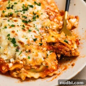 Skillet lasagna made with ravioli on plate with fork scooping up a forkful.