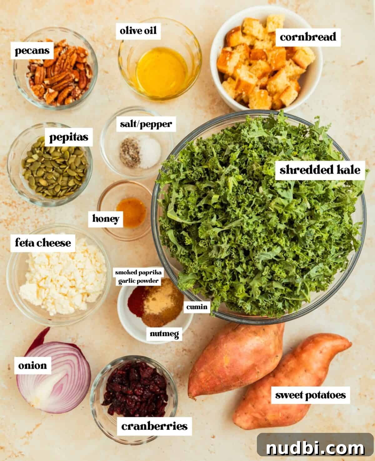 Roasted Sweet Potato and Kale Salad with Maple Dijon Dressing 4 Shredded kale in glass bowl, cornbread cubes, feta, sweet potatoes, and other ingredients on surface.
