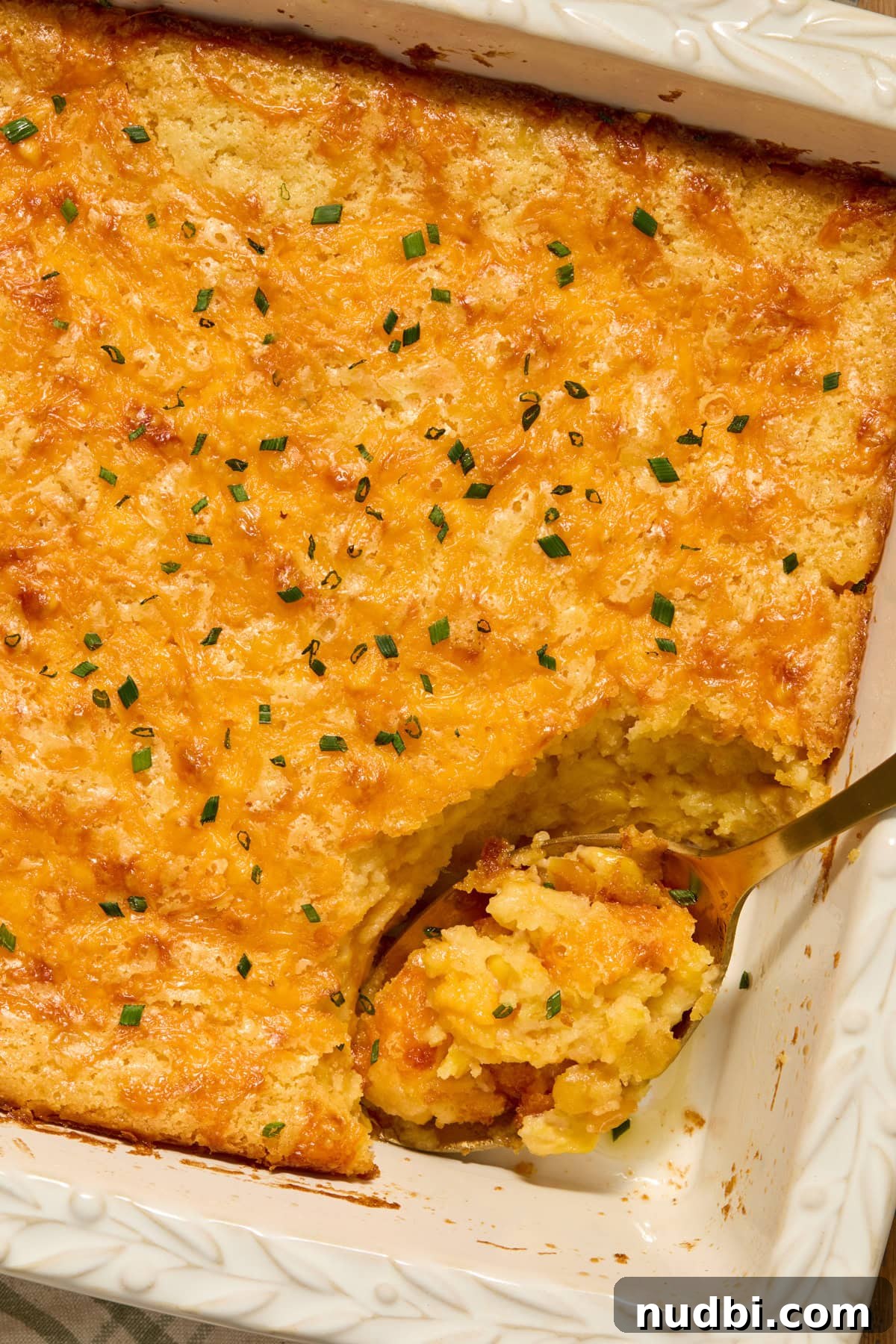 Dish with serving spoon scooping into corn casserole topped with chopped chives.