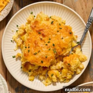 Cheesy cornbread casserole on white dish with fork scooping in.