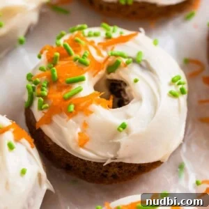 Carrot cake donut with cream cheese icing topped with sprinkles and shredded carrots.