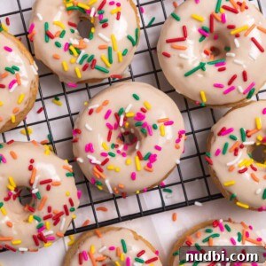 Vanilla baked donuts with maple glaze and rainbow sprinkles on cooling rack.