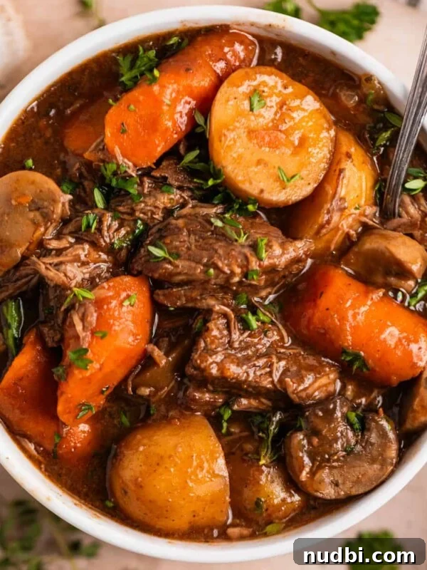 Slow Cooker Cheeseburger Soup Recipe for Weeknight Dinners 11 White bowl with crockpot beef stew with mushrooms, carrots and potatoes topped with chopped parsley.