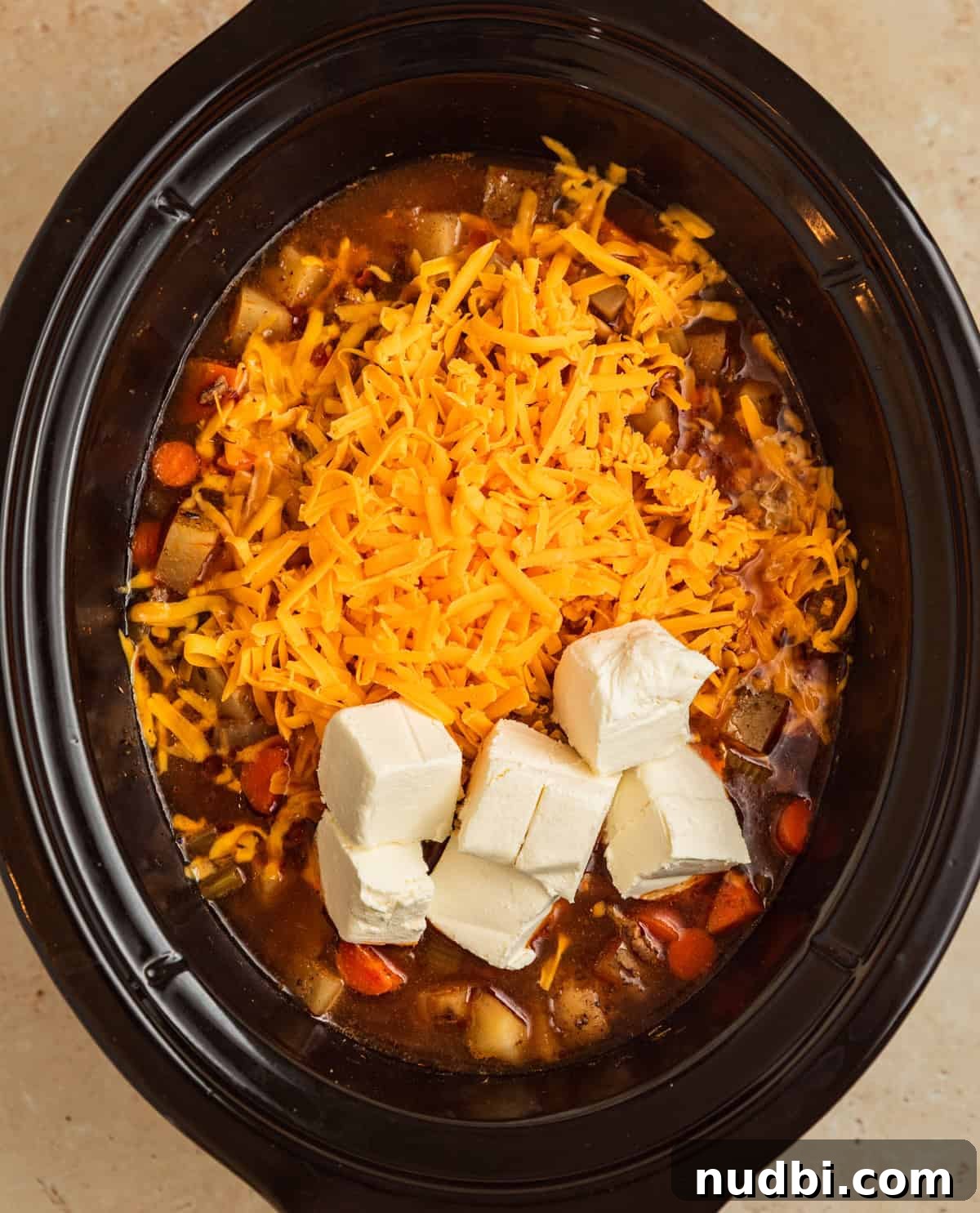 Slow Cooker Cheeseburger Soup Recipe for Weeknight Dinners 9 Shredded cheddar cheese and cubed cream cheese added to crockpot soup.