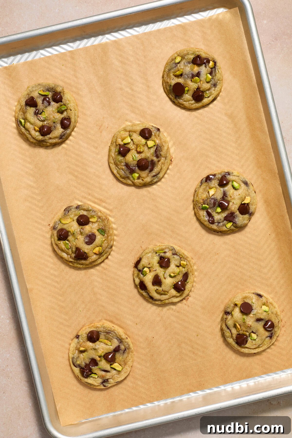 Chewy Pistachio Chocolate Chip Cookies Recipe for Home Bakers 14 Freshly baked cookies on parchment lined baking sheet.