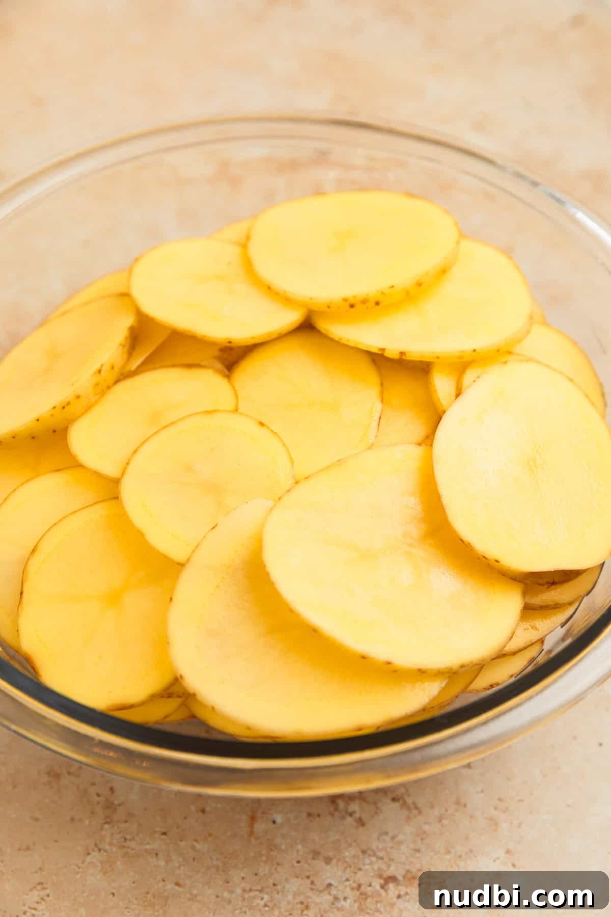 Creamy Gruyère Scalloped Potatoes with Garlic and Thyme 5 Sliced potatoes in glass mixing bowl.