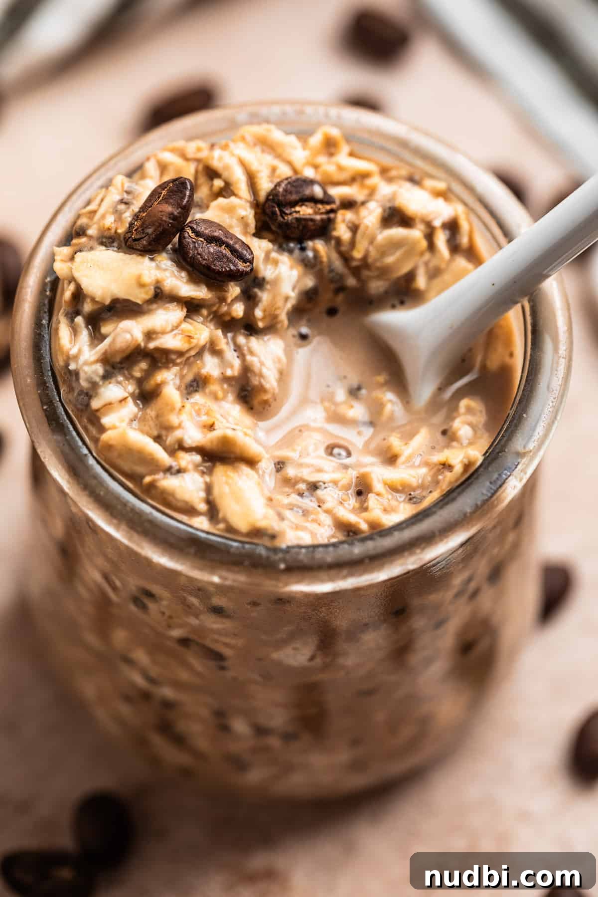 Vanilla Cold Brew Overnight Oats Recipe for Creamy Morning Energy 4 Coffee overnight oats with white spoon scooping into jar and coffee beans on top.