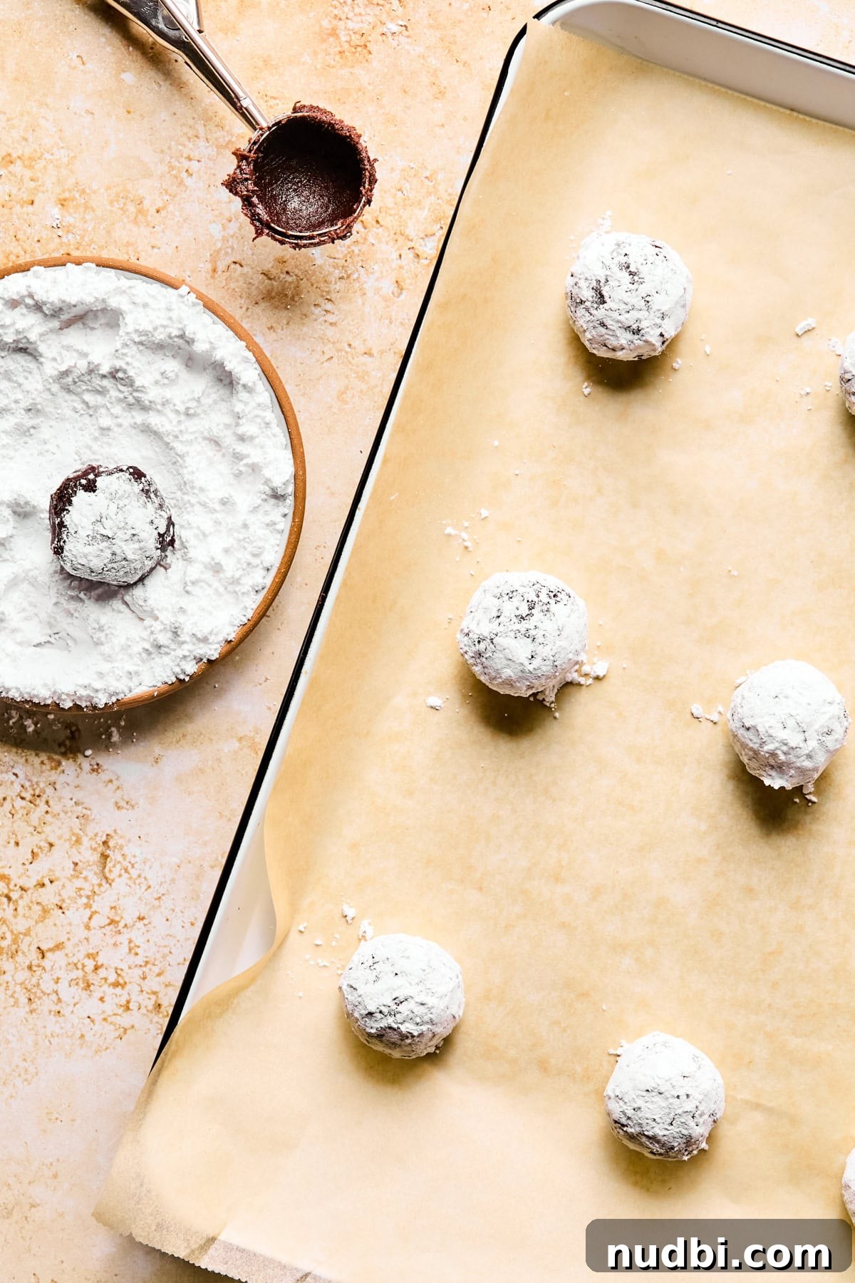 Brownie Crinkle Cookies Recipe — Fudgy, Chewy Chocolate Treats 7 Parchment lined pan with chocolate crinkle cookie dough balls rolled in powdered sugar.