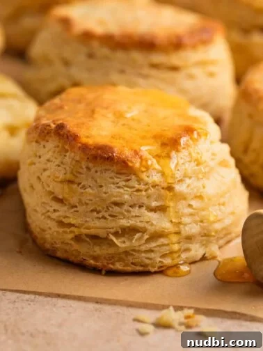 Simple honey biscuits on tan parchment with honey drizzling over top with honey dipper stick beside it.