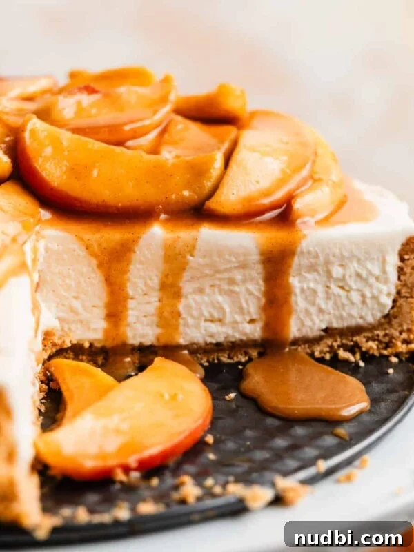 No-Bake Mini Biscoff Cheesecakes Recipe for Crowd-Pleasing Treats 19 Cheesecake on cake stand with slice cut out to expose the texture of the cheesecake with caramel apples on top.