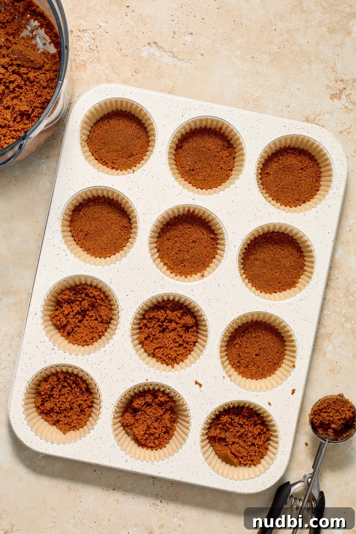 No-Bake Mini Biscoff Cheesecakes Recipe for Crowd-Pleasing Treats 7 Biscoff cookie crust being pressed into muffin tin.