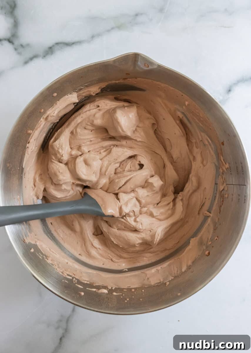 Light and Fluffy Chocolate Whipped Cream Recipe 5 Chocolate whipped cream with stiff peaks in bowl with gray spatula.