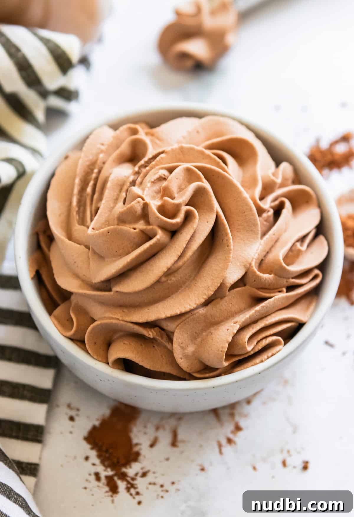 Light and Fluffy Chocolate Whipped Cream Recipe 8 Piped chocolate whipping cream in white bowl with cocoa powder dusted around it.