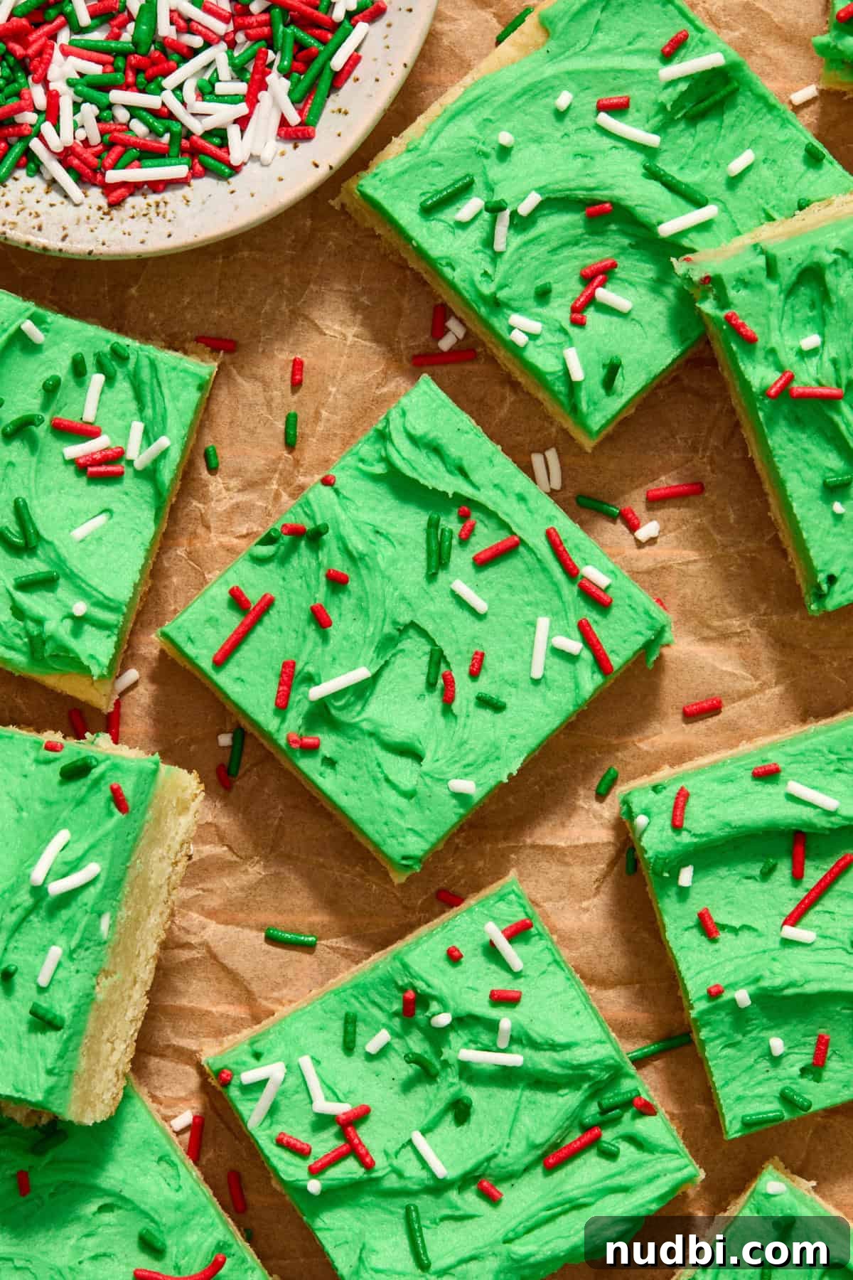 Christmas Sugar Cookie Bars Recipe with Festive Frosting 15 Sugar cookie bars on parchment with green frosting and Christmas color sprinkles.