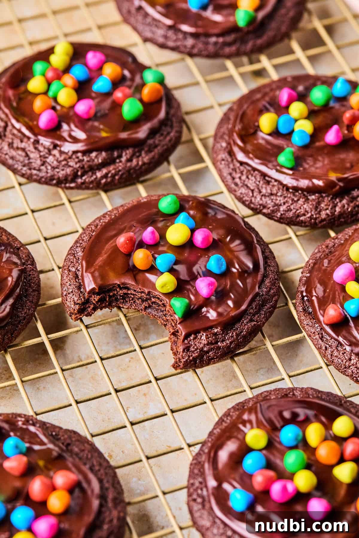 Cosmic Brownie Cookie Recipe: Fudgy, Colorful Chocolate Cookies 15 Chocolate cookies with ganache and rainbow chips on top on wire rack.