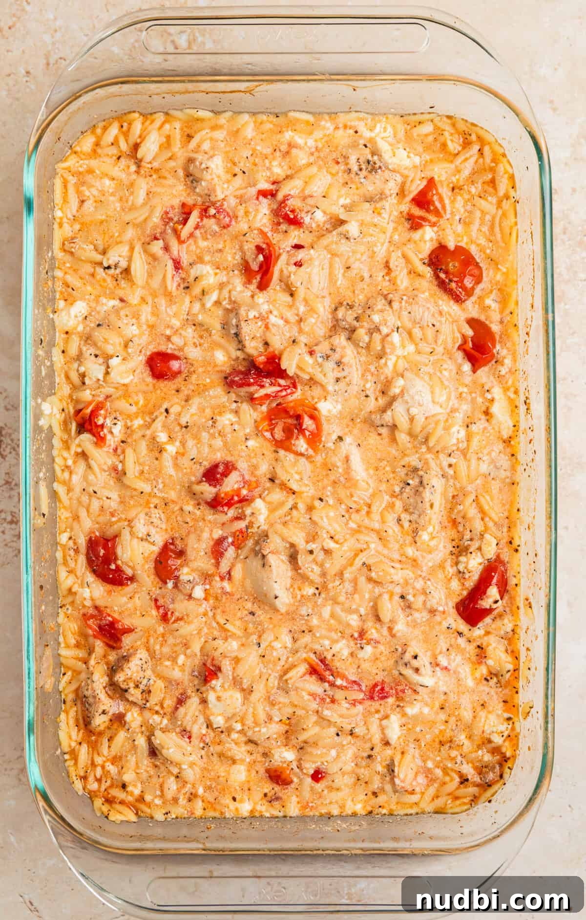 Greek Chicken with Lemon Orzo Pilaf: Flavorful Mediterranean Recipe 8 Feta mixed into Greek chicken and orzo bake in glass dish.