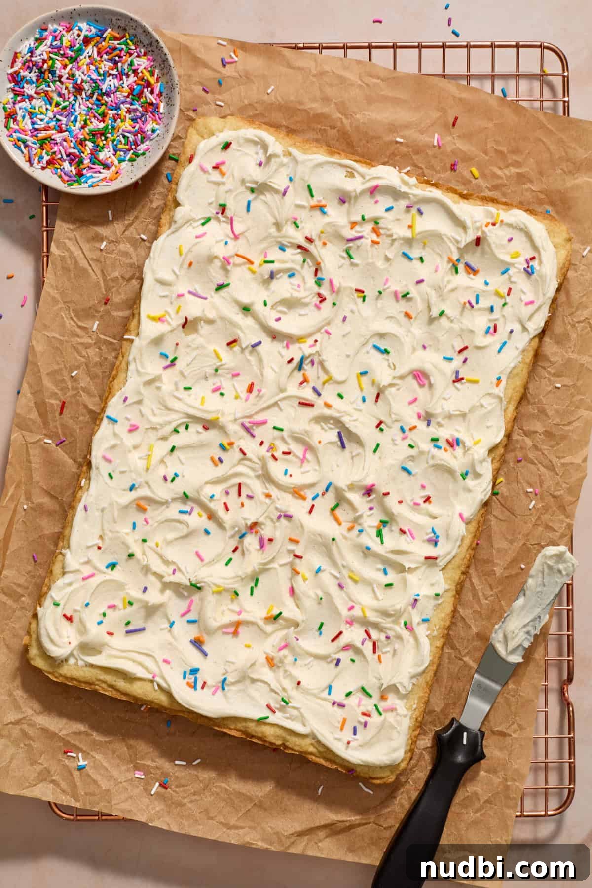 Frosted Sugar Cookie Bars Recipe — Soft, Chewy Dessert Bars 12 Frosted sugar cookie bars on parchment with sprinkles.