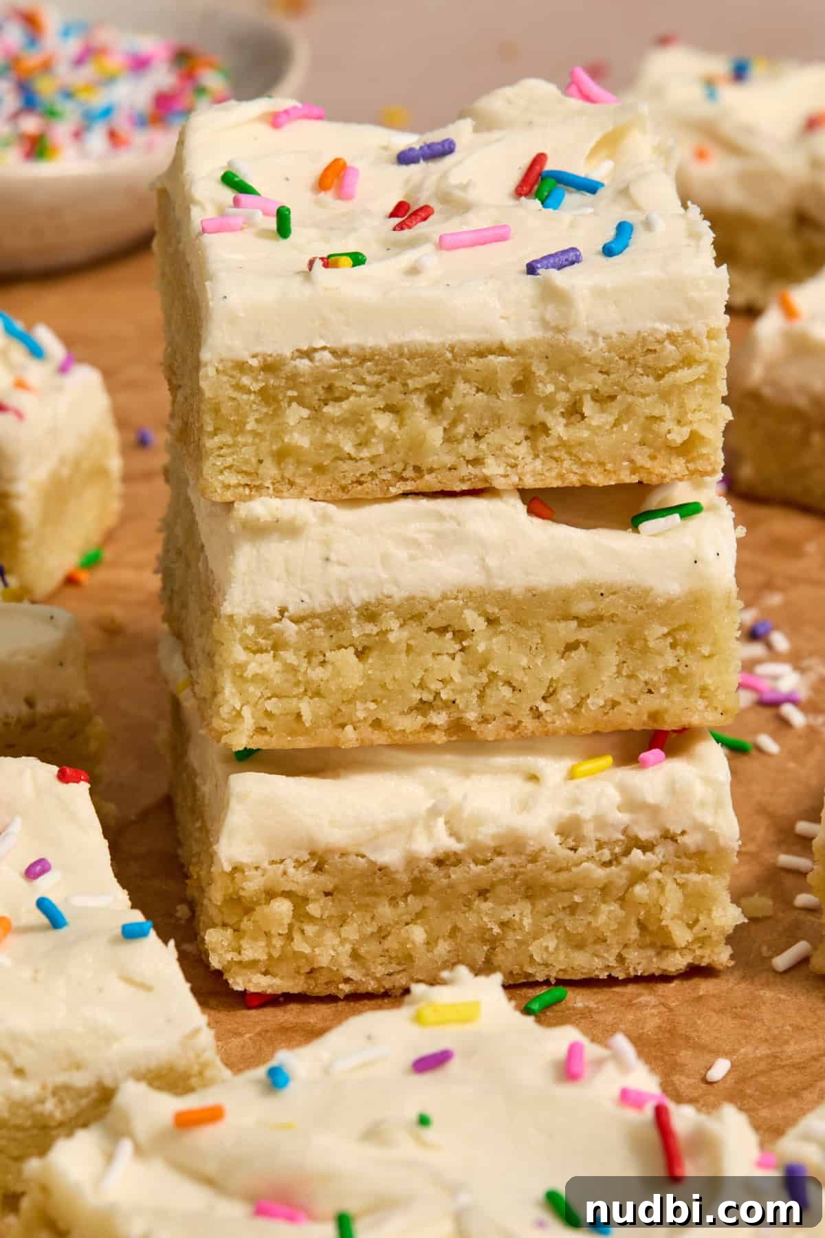 Frosted Sugar Cookie Bars Recipe — Soft, Chewy Dessert Bars 13 Stack of sugar cookie bars with frosting and sprinkles.