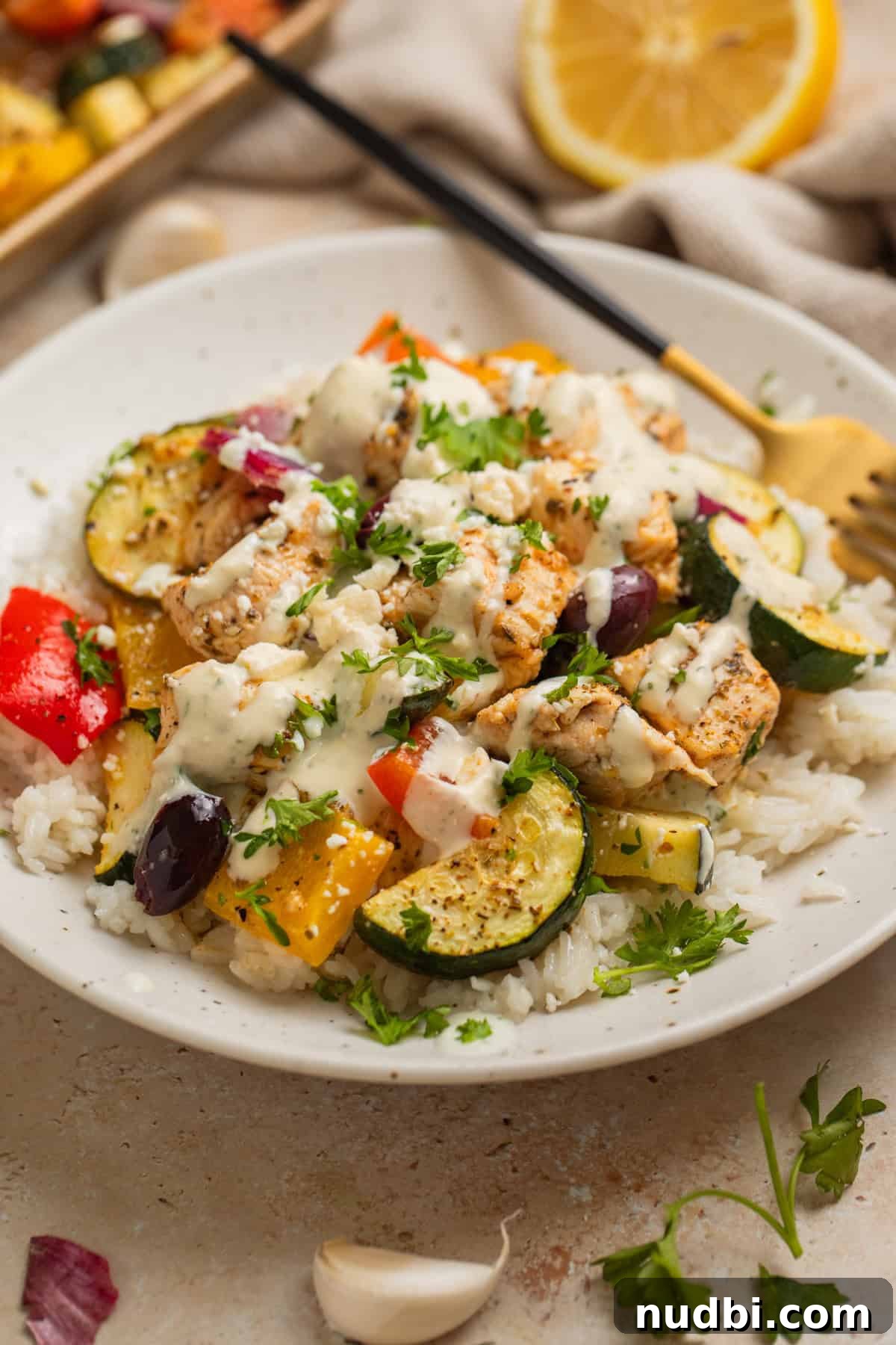 Greek-Style Sheet Pan Chicken Dinner with Lemon & Olives 11 Plate with seasoned chicken and vegetables topped with creamy feta sauce.