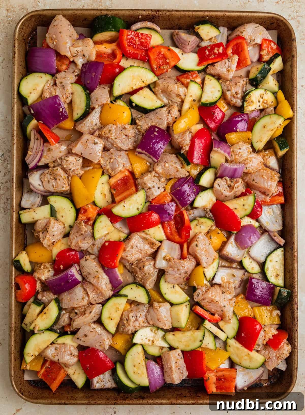 Greek-Style Sheet Pan Chicken Dinner with Lemon & Olives 7 Marinated cubed chicken and vegetables on baking sheet before cooking.