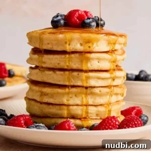 Fluffy Dairy-Free Pancakes: Simple Vegan Breakfast Recipe 7 Stack of pancakes topped with berries and maple syrup being poured from above.