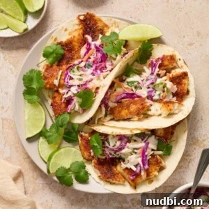Air fryer fish tacos topped with cilantro lime slaw on plate with lime wedges.