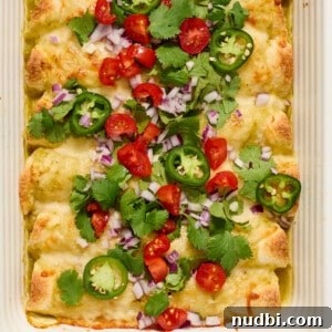 Pan of green chicken enchiladas topped with onion, cilantro, tomatoes, etc.