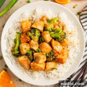 Orange chicken and broccoli served over white rice on plate.