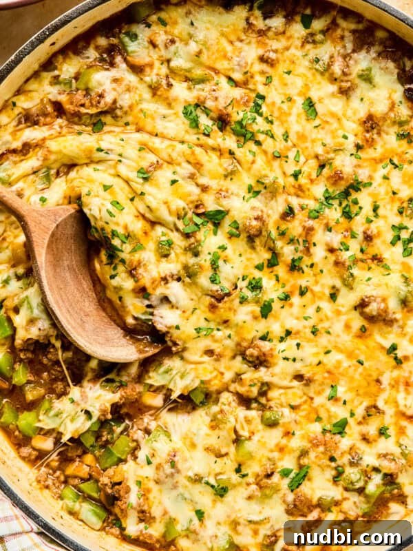 Cheese topped Philly cheesesteak skillet mixture in pan with wood spoon.