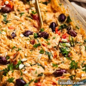 Creamy feta baked chicken and orzo topped with olives, parsley and basil in pan.