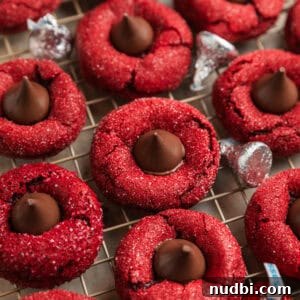 Red Velvet Blossom Cookies Recipe — Soft, Cream Cheese Frosting 12 Red velvet cookies with Hershey kiss centers on wire rack.